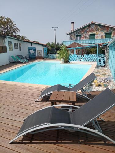 a swimming pool with a table and chairs next to it at La Maison Mosaic Medoc - Gîtes in Gaillan-en-Médoc