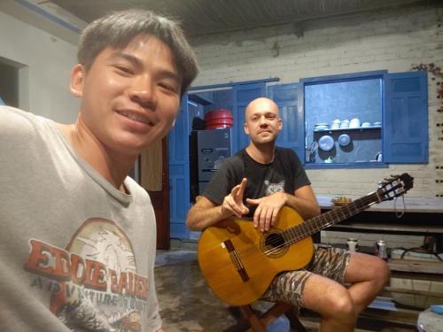 a man playing a guitar with a man sitting on a chair at nhà Ba cơm Má in Phương Phi