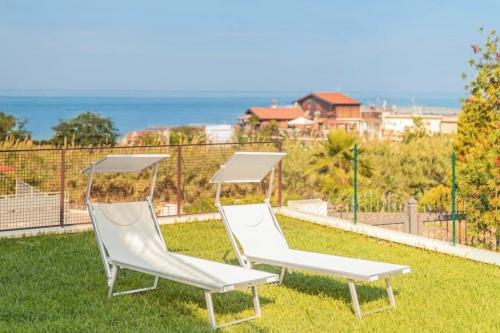 2 chaises blanches assises au-dessus de l'herbe dans l'établissement Nacàri Home, à Giardini Naxos