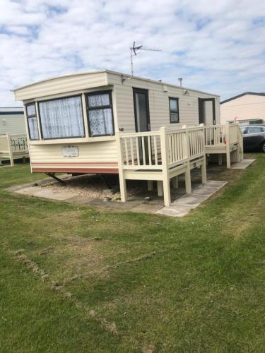 a small yellow caravan with a porch and a yard at A4 THE CHASE 6 Berth Pet Friendly Caravan With Decking in Ingoldmells