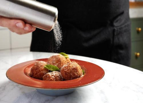 a person sprinkling sugar on a plate of food at Virgin Hotels New Orleans in New Orleans