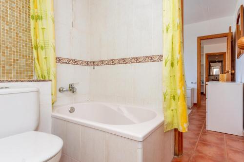 baño con bañera, aseo y cortinas amarillas en Villa Elfa, en Cala en Forcat