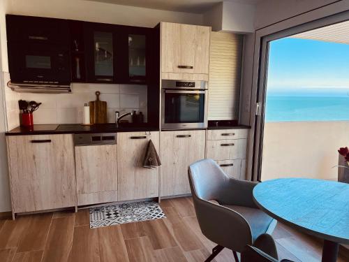 een keuken met houten kasten en een tafel en uitzicht op de oceaan bij Studio, vue mer à 150m de la plage in Trouville-sur-Mer