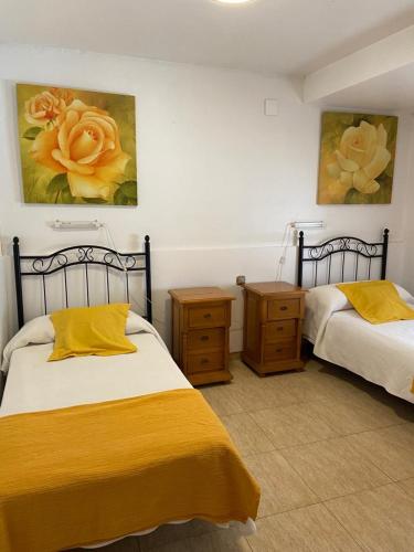 1 dormitorio con 2 camas con sábanas amarillas y pinturas en Pensión Santa Rita, en Calatayud
