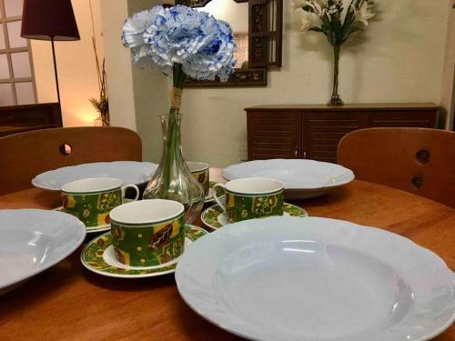 una mesa con platos y tazas y un jarrón con flores en JUST NICE ,Selesa hillhome bukit tinggi bentong, en Bentong