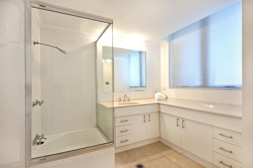 a white bathroom with a shower and a sink at Berkeley on the Beach in Gold Coast
