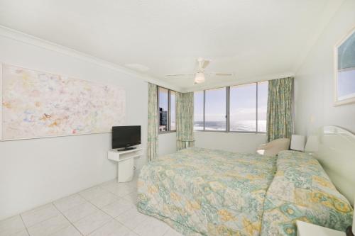a bedroom with a bed and a tv and windows at Berkeley on the Beach in Gold Coast
