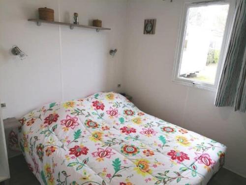 Una cama en una habitación con una manta de flores. en Le balaou, en Lit-et-Mixe