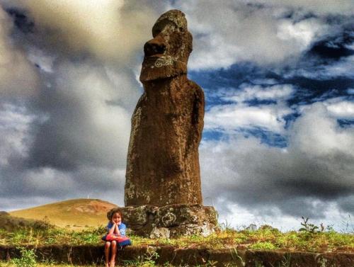 a young girl sitting in front of a statue at Kahina Lodge in Hanga Roa