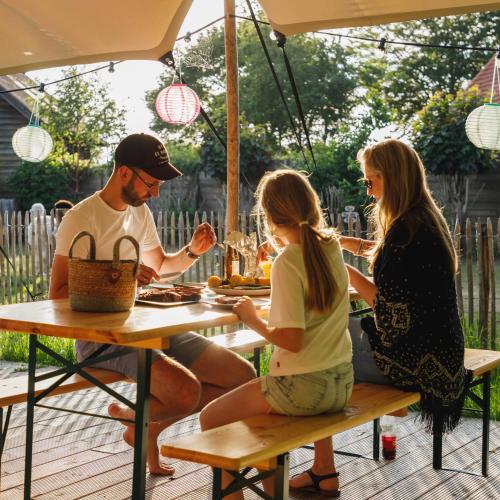 three people sitting at a table under an umbrella at Wereldse Bell Tenten met alpaca's in Paasloo