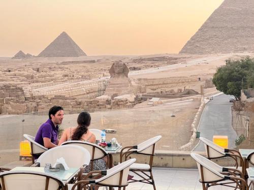 twee mensen die aan een tafel zitten en naar de piramides kijken bij Pyramids Valley Boutique Hotel in Caïro