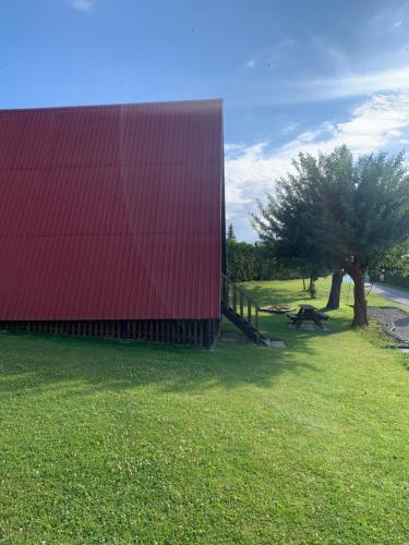 un edificio rojo en un campo con un árbol en "Domek na Wiejskiej 4" Polańczyk , 696-025-331, en Polańczyk