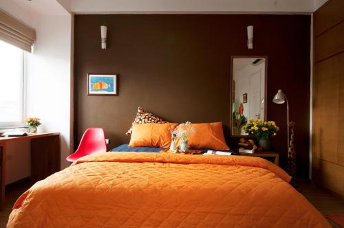 Chez Tram Homestay في هانوي: غرفة نوم بسرير برتقالي وكرسي احمر
