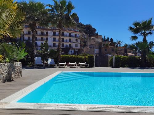 a swimming pool in front of a building with palm trees at Taormina Art Apartment by Taormina Holidays in Taormina