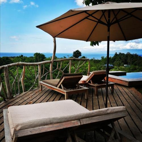 a wooden deck with two chairs and an umbrella at Nakabalo Guesthouse & Restaurant in Siquijor