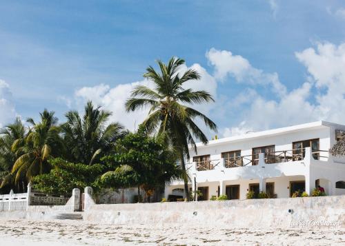 un edificio bianco sulla spiaggia con palme di Uroa Zanzibar Vera Beach Hotel by Moonshine a Dikoni