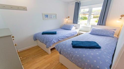a bedroom with two beds with blue sheets and a window at Swallows Croyde - Open plan beach chalet & close proximity to the beach - Sleeps 6 in Croyde