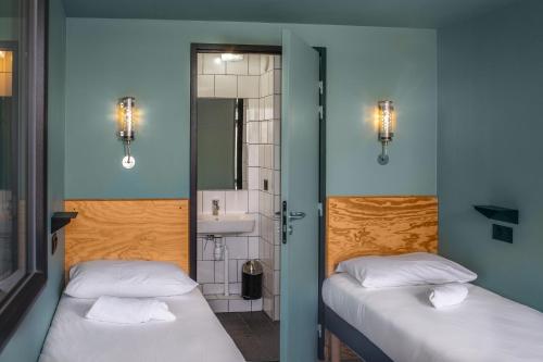 two beds in a room with a bathroom with a sink at Eklo Toulouse in Toulouse