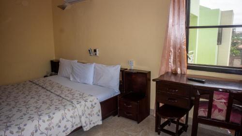 a bedroom with a bed and a desk and a window at Pekan Hotel in Accra
