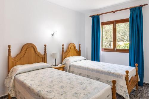 two beds in a bedroom with blue curtains and a window at Calamar 7 in Portocolom