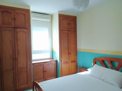 1 dormitorio con cama, ventana y armarios de madera en Chalet adosado con azotea andaluza y patio, junto a la playa, en Isla Cristina