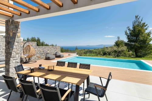 a patio with a wooden table and chairs next to a swimming pool at Koni Villas Agia Paraskevi by Halkidiki Villas in Agia Paraskevi