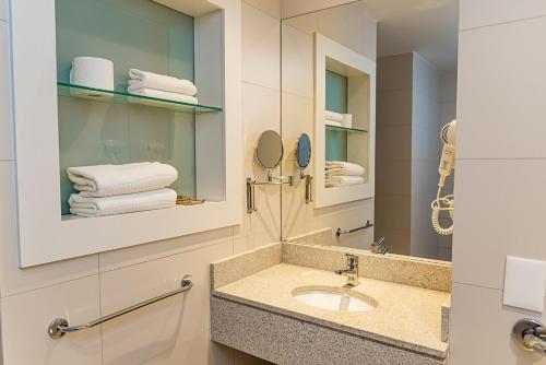 een badkamer met een wastafel, een spiegel en handdoeken bij Rio Hotel by Bourbon Maringá in Maringá