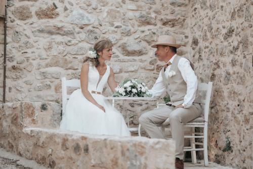 a bride and groom sitting on a bench in front of a stone wall at The Aegean blue country house Old Milos in Lagoúdi Zía