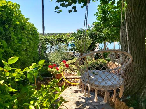 a swing in a garden with flowers and a chair at APARTMAN VINKO in Barbat na Rabu