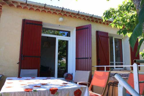 eine Terrasse mit roten Türen sowie einem Tisch und Stühlen in der Unterkunft À l'ombre du mûrier in Blauvac