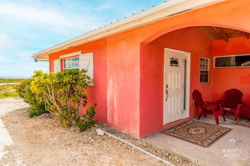 a red house with a white door and a table and chairs at Chalk Sound Beach Residences Near Sapodilla Bay Beach by Angel Host! in Providenciales