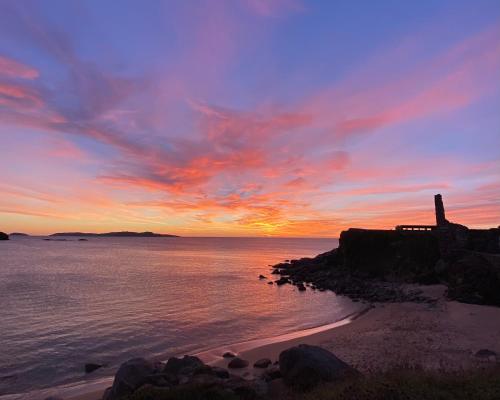 a sunset over the ocean with a lighthouse on the shore at Duerming Areas Playa Hotel in Sanxenxo