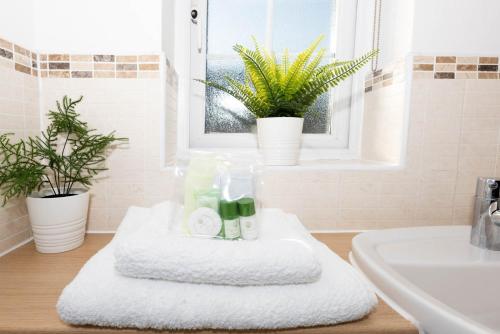 a bathroom with white towels and plants on a counter at Riverside Stays, Modern House Stays, Shefford, Bedfordshire in Shefford
