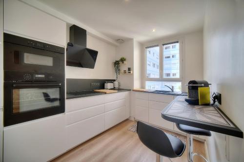 La cuisine est équipée de placards blancs et d'un four avec plaques de cuisson noires. dans l'établissement IMMOGROOM - Spacieux 3 pièces - Garage - Terrasse - Climatisation, à Cannes