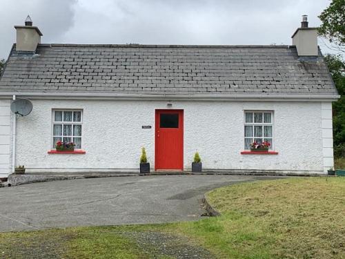 a white house with a red door and two windows at Butler's Cottage, Letterkenny in Letterkenny