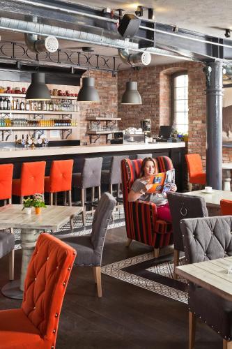 a woman sitting in a chair reading a book in a restaurant at Hotel Browar Kościerzyna in Kościerzyna