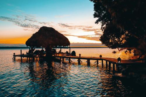 a dock with a straw umbrella on the water at sunset at La Lancha in El Remate