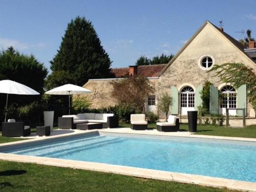 - une piscine avec des chaises et des parasols en face d'une maison dans l'établissement Le Clos des Aubrys, à Châteauroux