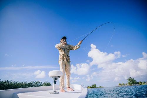 a man standing on a boat holding a fishing rod at Turtle Inn by Francis Ford Coppola in Placencia Village