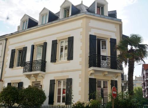 een wit huis met zwarte luiken en een palmboom bij Maison Garnier Hôtel de Charme Biarritz in Biarritz