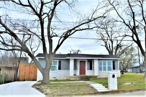 a white house with a red door and trees at Cozy Haus Relaxing 'Home Base' WiFi Location Close to Town and Rivers, Schlitterbahn, Gruene in New Braunfels