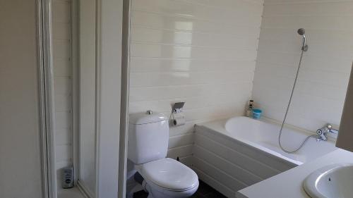 een witte badkamer met een toilet en een bad bij Bungalow de Pluumpot in Scherpenisse