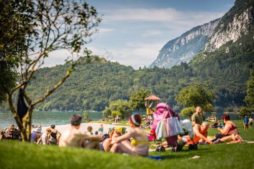 a group of people sitting on the grass near a lake at Hotel Arcobaleno in Fai della Paganella