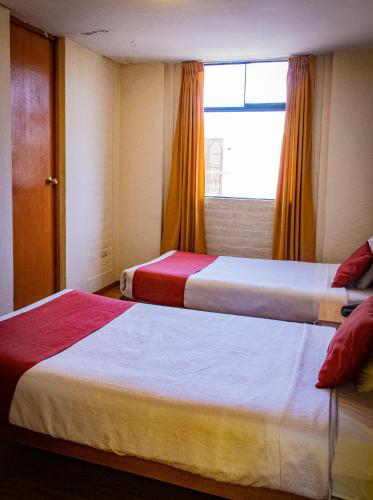 two beds in a hotel room with a window at Hotel La Posada de Ugarte in Arequipa