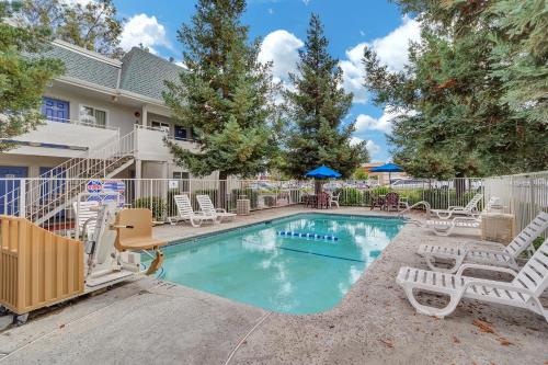 a swimming pool with white chairs and tables and trees at Motel 6-Rohnert Park, CA in Rohnert Park