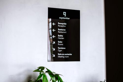 a black sign on a white wall with a plant at Hotel Septembar in Podgorica