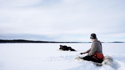 a man and a dog sitting in the snow at Heteranta, Lake Inari / Inarijärvi in Inari