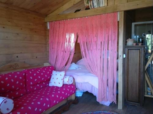 a bedroom with a bed with pink curtains and a couch at Chalet sur Pilotis Ane'ita de l'Arbenquens in La Mure