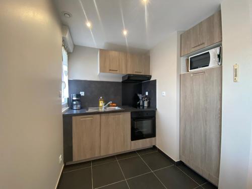 Elle comprend une petite cuisine avec des placards en bois et un évier. dans l'établissement Champêtre - Gîte entièrement neuf à 100 mètres de la plage, à Wimereux