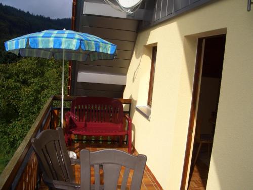 2 sillas y una sombrilla en el balcón en Ferienwohnung am Busterbach, en Seebach